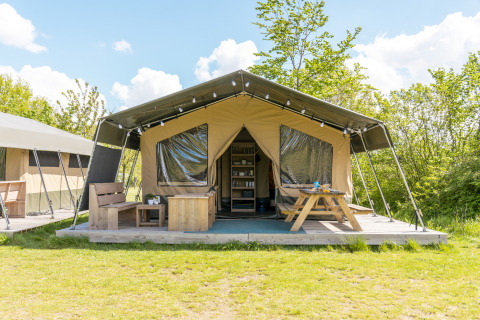 Safari tent at Camping De Betteld in the Netherlands with wooden deck, bench, and picnic table outside.