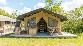 Safari telt på Camping De Betteld i Holland med træterrasse, bænk og picnicbord under solrige himmel.