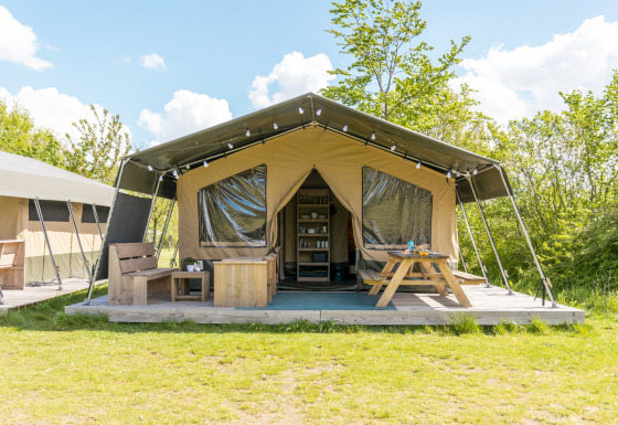 Safari-Zelt auf dem Campingplatz De Betteld in den Niederlanden mit Holzterrasse, Bank und Picknicktisch.