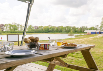 Colazione all'aperto su tavolo da picnic vicino a lago, tenda safari, Camping De Betteld, Paesi Bassi.