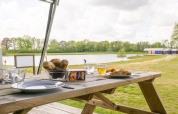 Outdoor breakfast at a picnic table by a lake, safari tent, Camping De Betteld, Netherlands, scenic view.
