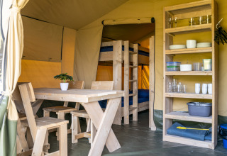 Interior de una tienda safari con mesa y sillas de madera en Camping De Betteld, Países Bajos.