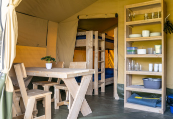 Interno di tenda safari con tavolo, sedie in legno e scaffale al Camping De Betteld nei Paesi Bassi.