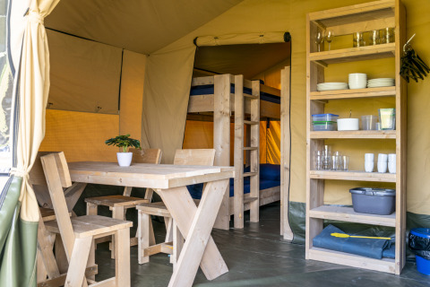 Interieur van een safaritent met houten tafel, stoelen en rek op Camping De Betteld in Nederland.
