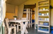 Interior of a safari tent with wooden table, chairs, shelving and bunk beds at Camping De Betteld.