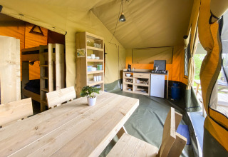 Interior de una tienda safari en Camping De Betteld, Países Bajos, con cocina, mesa y literas visibles.
