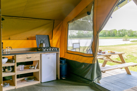 Cocina de tienda safari en Camping De Betteld, Países Bajos, con vistas al lago y mesa de picnic.