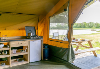 Cucina in tenda safari al Camping De Betteld nei Paesi Bassi, con vista sul lago e tavolo da picnic.