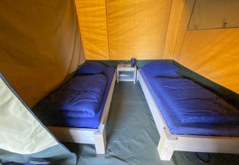 Interior de una tienda safari en Camping De Betteld, Países Bajos, con dos camas individuales y ropa de cama azul.