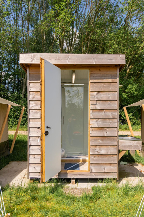 Kleines Holzhaus mit geöffneter Tür und Badezimmereinrichtung, Camping De Betteld, Niederlande.