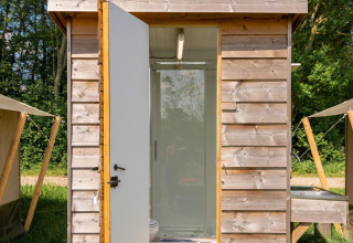 Petite cabane en bois avec porte ouverte révélant une salle de bain, au Camping De Betteld, Pays-Bas.
