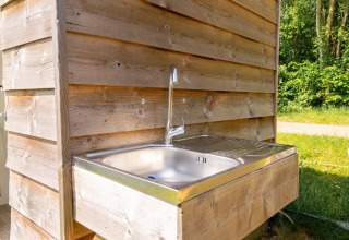 Évier extérieur près d’une tente safari au Camping De Betteld, Pays-Bas, avec mur en bois et verdure.