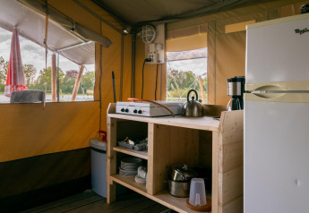 Cucina in tenda safari con fornello, bollitore e frigorifero a Camping De Betteld, Paesi Bassi, vista natura.