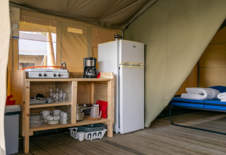 Binnenaanzicht van een safaritent op Camping De Betteld in Nederland met keuken en bed zichtbaar.