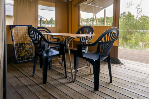 Tenda safari al Camping De Betteld nei Paesi Bassi, con sedie di plastica e tavolo di legno su terrazza.