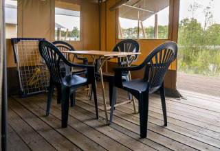 Tienda safari en Camping De Betteld (Países Bajos) con sillas de plástico y mesa de madera en la terraza.