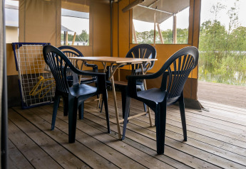 Tenda safari al Camping De Betteld nei Paesi Bassi, con sedie di plastica e tavolo di legno su terrazza.