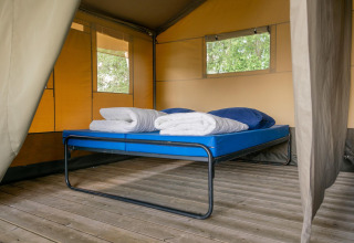 Vista interna di una tenda safari con letto e pavimento in legno al Camping De Betteld nei Paesi Bassi.