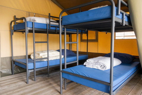 Interior de una tienda safari en Camping De Betteld, Países Bajos, con literas y ropa de cama preparada.