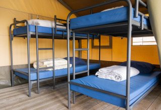 Interior de una tienda safari en Camping De Betteld, Países Bajos, con literas y ropa de cama preparada.