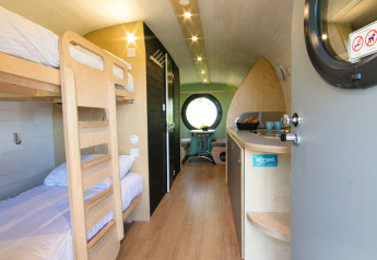 Vista interior de una pequeña casa con literas, cocina pequeña y ventana redonda en los Países Bajos.