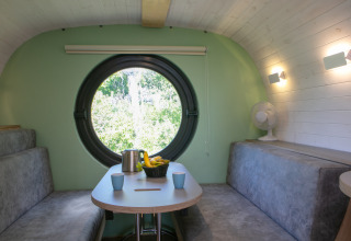 Binnenkant van de Anthropod tiny house in Holiday Park 't Rheezerwold, Nederland, met rond raam en zitjes.