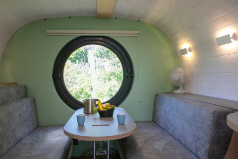 Inde i et lille hus kaldet Anthropod i Holiday Park 't Rheezerwold, Nederlandene, med rundt vindue og moderne sofaer.