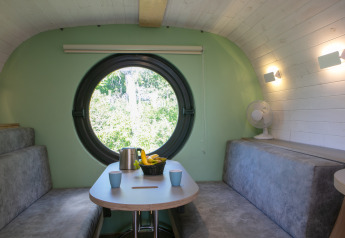 Interieur van tiny house Anthropod op Holiday Park 't Rheezerwold in Nederland, met rond raam en zitbanken.