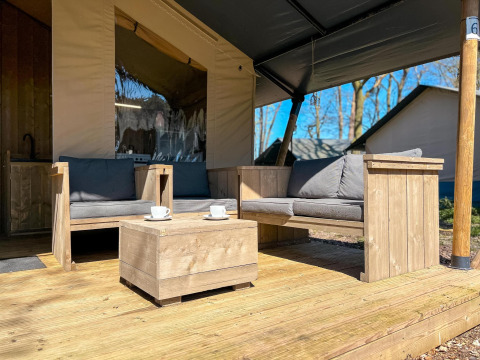 Tenda safari di lusso con mobili in legno sulla veranda al Camping De Betteld nei Paesi Bassi, soleggiato.
