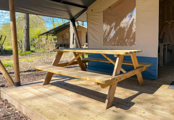 Udendørs picnicbord på en træterrasse ved en luksus safaritelt med sanitære faciliteter i Camping De Betteld.
