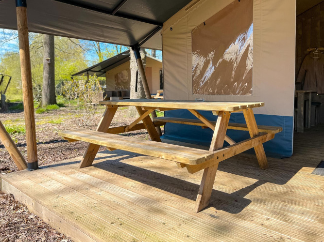 Picknicktisch aus Holz auf einer Terrasse vor einem Luxuszelt mit Sanitäranlagen auf Camping De Betteld.