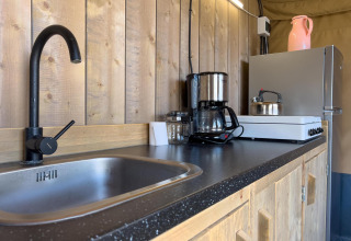 Kitchen area in a luxury safari tent at Camping De Betteld, featuring sink, stovetop, and coffeemaker.