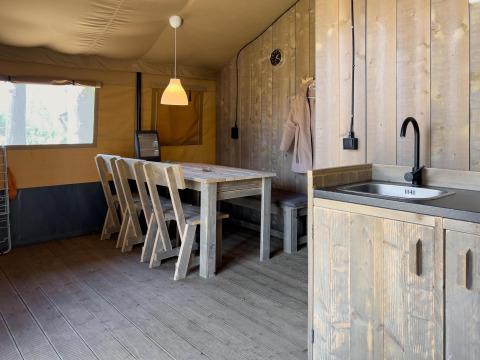 Interno di una tenda safari di lusso con tavolo da pranzo, sedie e angolo cottura al Camping De Betteld, Paesi Bassi.