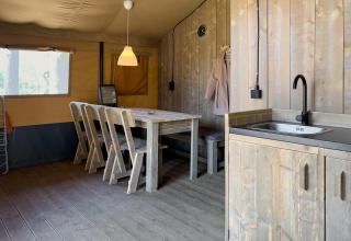 Interior de una tienda safari de lujo con mesa de comedor, sillas y cocina en Camping De Betteld, Países Bajos.