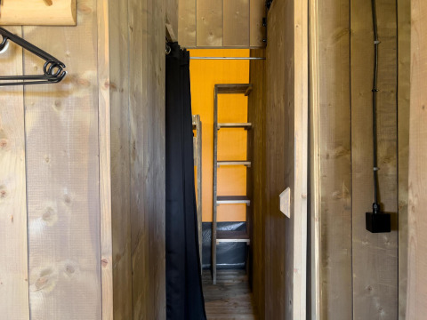 Pasillo estrecho de una tienda safari de lujo en Camping De Betteld, Países Bajos, con paredes de madera y escalera.