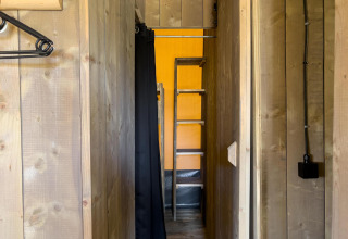 Smal gangetje in een luxe safaritent op Camping De Betteld, Nederland, met houten muren en ladder.