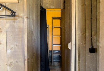 Corridoio stretto in una tenda safari di lusso al Camping De Betteld, Paesi Bassi, con pareti in legno e scala.