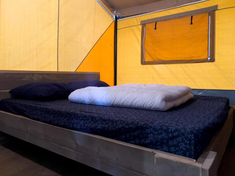 Interno di una tenda safari di lusso con letto matrimoniale e pareti gialle al Camping De Betteld, Olanda.