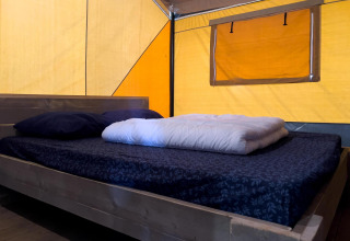 Binnenkant van een luxe safaritent met tweepersoonsbed en gele wanden bij Camping De Betteld, Nederland.