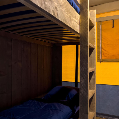 Habitación de tienda safari de lujo con literas en Camping De Betteld, Países Bajos, con cálida iluminación.