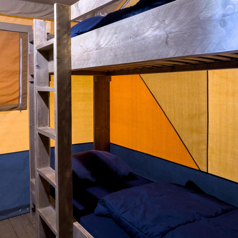 Letto a castello in legno con biancheria scura in una tenda safari di lusso al Camping De Betteld, Paesi Bassi.