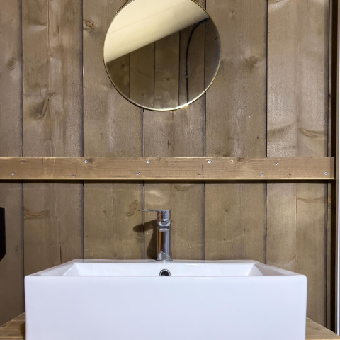 Lavabo moderno in tenda safari di lusso al Camping De Betteld, Paesi Bassi, con parete in legno e specchio.