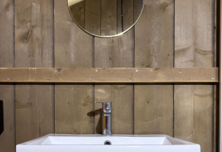 Moderne wastafel in een luxe safaritent op Camping De Betteld, Nederland, met hout en een ronde spiegel.