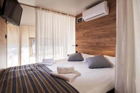 Inviting bedroom at Lodge Kiezel, Zilverstrand, Belgium featuring a double bed, TV, air conditioning, and wood wall.