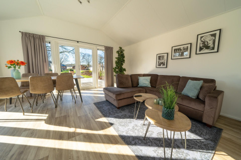 Helles, modernes Wohnzimmer in der Velthorst-Lodge im Zilverstrand, Belgien, mit Sofa, Esstisch und großen Fenstern.