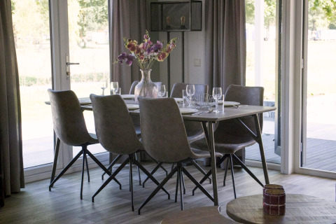 Table à manger avec six chaises et un vase de fleurs à la lodge Velthorst à Zilverstrand, Belgique, décor lumineux.