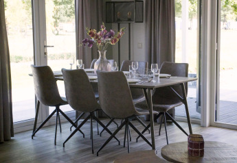 Table à manger avec six chaises et un vase de fleurs à la lodge Velthorst à Zilverstrand, Belgique, décor lumineux.