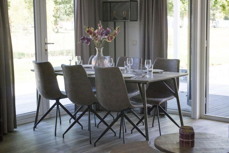 Dining table with six chairs and a flower vase at Velthorst lodge in Zilverstrand, Belgium, bright setting.
