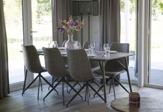 Esstisch mit sechs Stühlen und Blumen in einer Vase in der Velthorst-Lodge am Zilverstrand in Belgien.