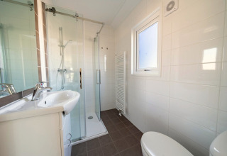 Salle de bain moderne au lodge Velthorst à Zilverstrand, Belgique, avec douche, lavabo et fenêtre.
